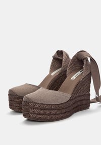 Le zeppe espadrillas marroni presentano una tomaia in tessuto testurizzato, una piattaforma intrecciata in juta e lacci in tessuto alla caviglia. Punta liscia e forma arrotondata.