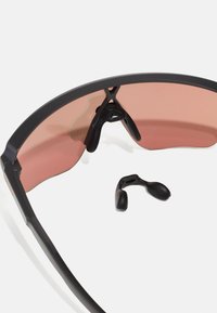 Sonnenbrille mit einem schwarzen Kunststoffrahmen und rosa getönten Gläsern. Enthält schwarze Gummi-Nasenpads. Die gebogene Form verbessert den Schutz.