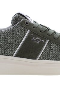 Grön texturerad sneaker med vita accenter, med ett vävt mönster, perforerad panel och U.S. Polo Assn. logo på sidan.