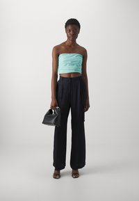 Haut sans manches bleu-vert raccourci avec une texture froncée, associé à un pantalon large bleu marine et un sac à main noir. Tissu lisse, design minimaliste.