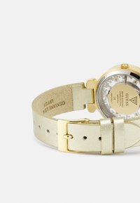 Goldfarbene Uhr mit einem metallischen, hellgoldenen Lederarmband. Das Armband verfügt über eine Schnallenverschluss und ist mit "Echtleder" geprägt.