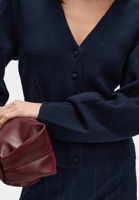 Granatowy, dzianinowy kardigan z dekoltem w serek, trzema guzikami i długimi rękawami. Połączony z bordową, miękko teksturowaną skórzaną kopertówką.