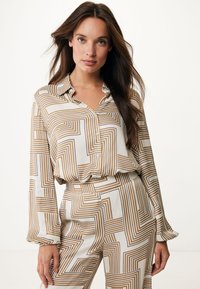 Blusa donna a maniche lunghe color crema con motivo geometrico marrone, dotata di colletto e chiusura con bottoni, realizzata in un tessuto morbido.
