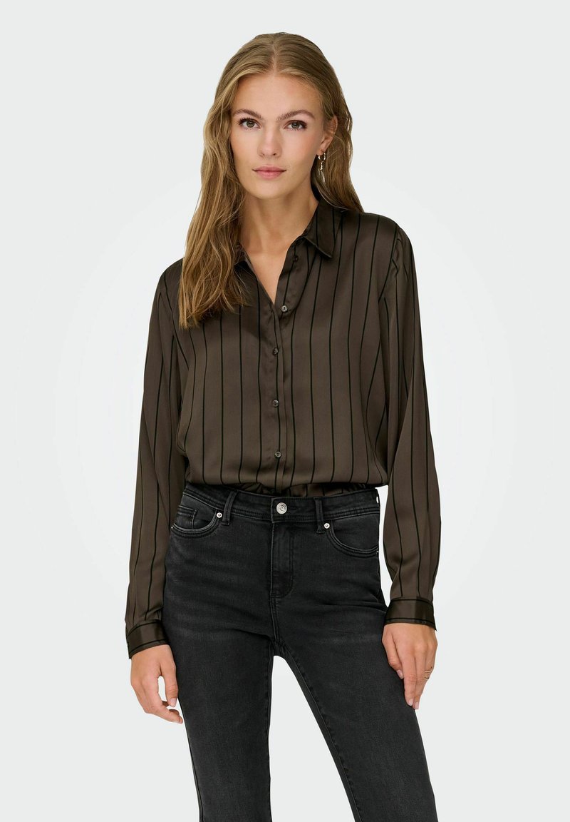 Blusa de manga larga de color verde oscuro con rayas verticales negras, un cierre frontal de botones y una textura suave y sedosa. Combinada con unos pantalones vaqueros negros de talle alto.