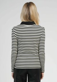 Polo shirt à manches longues rayé noir et blanc avec un col noir, arborant un design ajusté en tissu lisse. Coutures visibles aux épaules.