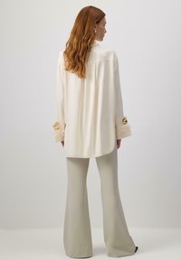 Blouse crème à manches longues, avec des poignets décorés et des accents dorés. Associée à un pantalon évasé vert clair. Texture lisse et douce.