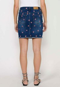 Denim mini krilo s prilegajočo zasnovo, cvetnim vezenjem in raztrganim robom. Zadnji žepi povečujejo uporabnost z klasično denim teksturo.