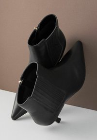 Černé kožené kotníkové boty s špičatou špičkou, elastickými postranními panely a malým podpatkem. Hladká textura s jemnými švy.