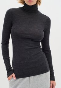 Dark gray turtleneck long-sleeve top with a slim fit. Soft, lightweight fabric with slight texture. Features a small brand logo at the hem.