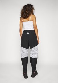 Černé kalhoty s bílými páskovanými vzory, elastickým pasem a zipovými manžetami. Vyrobeny z lehké tkaniny s volným střihem.