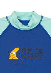 Långärmad rash guard i blått med mintgröna detaljer. Har en gul tecknad fiskgrafik och svart text som säger "BILLA BONG."