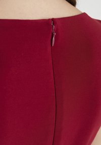 Lähikuva burgundivärise dressi seljapaelast, mida kannab inimene, kelle kael ja ülemine selg on avatud.