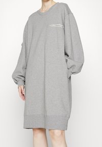 Överdimensionerad grå sweatshirtklänning med rundad hals, långa puffärmar, en frontficka med fransdetalj och ribbade manschetter.