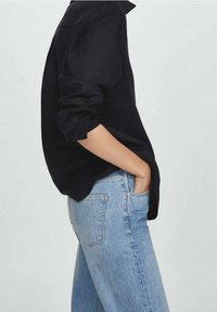 Chemise noire à manches longues avec poignets retroussés, associée à un jean taille haute bleu clair avec poches arrière et une texture denim classique.