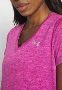 Camiseta deportiva melange rosa con diseño de cuello en V. Presenta un logo plateado de Under Armour en el pecho y mangas cortas. Textura suave.
