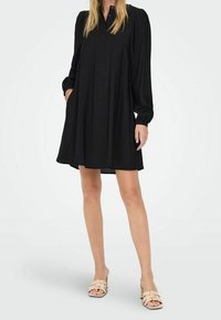 Czarna, luźno dopasowana sukienka z zapięciem na guziki i długimi rękawami, wykonana z miękkiego materiału. Posiada dwie boczne kieszenie i lekko bufiaste rękawy.