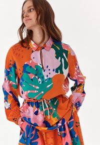 Färggjort, mönstrat skjorta med krage, som har abstrakta mönster i grönt, rosa och orange, samt en insydd midja med dragsko.