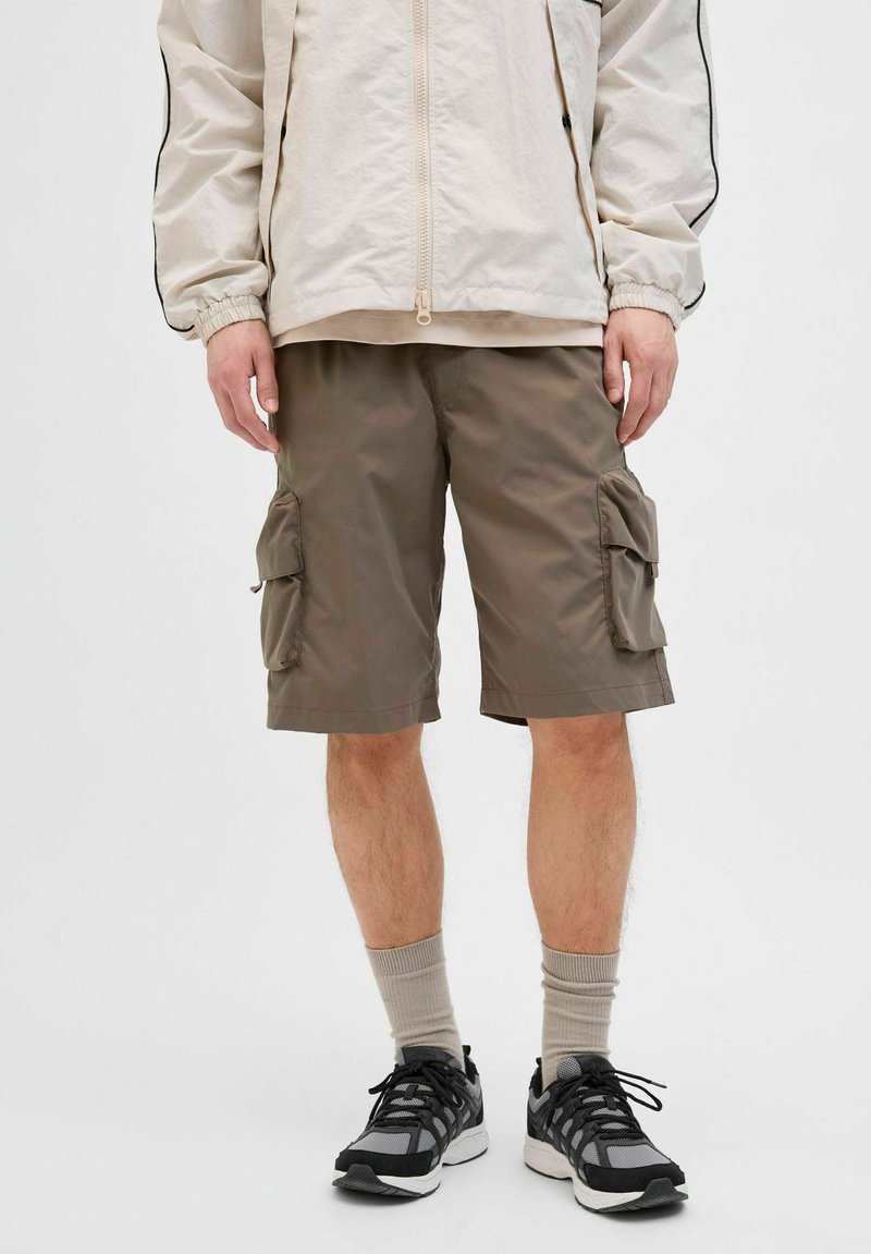 Olijfgroene cargoshorts, gemaakt van lichte stof, hebben twee zijzakken en een relaxte pasvorm, gecombineerd met zwarte sneakers en beige sokken.