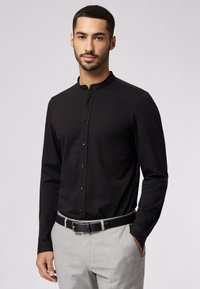 Zwarte overhemd met lange mouwen en een mandarin kraag, met een gladde textuur en subtiele glans. Gepaarde met grijze broek en een zwarte riem.