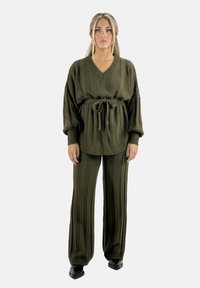 Conjunto de dos piezas tejido verde que presenta un suéter oversized a rayas con cuello en V y cinturilla con lazo, combinado con pantalones de pierna ancha.