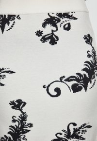 Bílá látka s černými květinovými vzory, obsahující spirály a složité detaily. Měkká textura a pletený design s přiléhavým pasem.