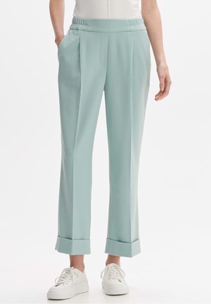 Persona vistiendo pantalones azul claro con puños y cintura elástica, y zapatillas blancas, de pie contra un fondo blanco liso.