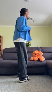 Blå krage skjorte som bæres over en hvit skjorte, grå joggebukser og svarte sneakers. En oransje plastisk blekksprut sitter på en mørk sofagruppe.