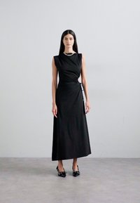 Rochie maxi neagră, fără mâneci, cu un design cu talie răsucită, textură netedă și minimalism în decorare. Purtați cu pantofi cu vârf ascuțit negri.