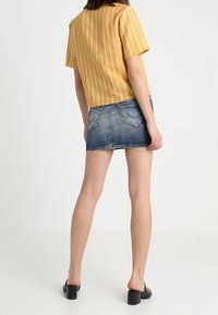 Gulrandig kortärmad topp i kombination med en blå denimminikjol. Svarta klackmules fulländar outfiten. Enkel design med en avslappnad look.