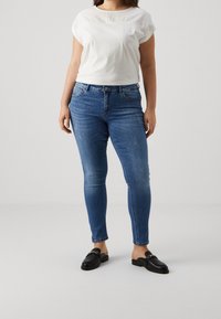 Vit t-shirt med texturerad detalj vid axlarna, i kombination med blå denim skinny jeans med en lätt blekning och svarta loafers.