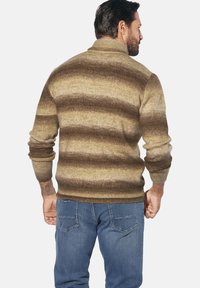 Gestrickter Pullover mit braun-beigen Farbverlaufsstreifen, ausgestattet mit hohem Kragen und gerippten Bündchen, kombiniert mit blauen Jeans.