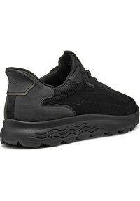 Zapatilla negra con parte superior de malla, acentos de cuero suave, cuello acolchado, suela texturizada y un distintivo patrón de tracción en forma de onda.