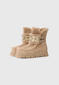 Stivaletti alla caviglia in finta pelliccia beige con una ampia fascia decorativa che presenta dettagli in tonalità dorata, cuciture e una suola in gomma spessa con un motivo a zigzag.