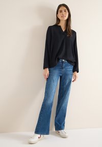 Czarna bluzka z długim rękawem i dekoltem w serek, zestawiona z szerokimi, niebieskimi dżinsami oraz białymi tenisówkami z czerwonymi akcentami. Minimalistyczny design, gładka faktura.