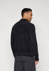 Schwarzer Pullover aus strukturiertem Strick mit hohem geripptem Kragen, langen Ärmeln und lockerem Schnitt, der eine weiche, flauschige Oberfläche und einen gerippten Saum zeigt.