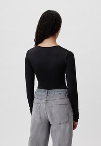 Černý dlouhý rukáv bodysuit s kulatým výstřihem, kombinovaný se světle šedými džíny s vysokým pasem, které mají dvě zadní kapsy a volný střih.