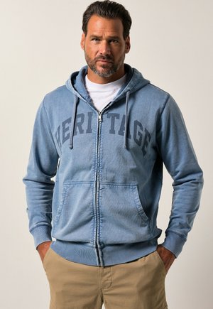 Light blue zip-up hoodie made of cotton blend, featuring a "HERITAGE" print, drawstring hood, and front pockets. Soft texture with ribbed cuffs.