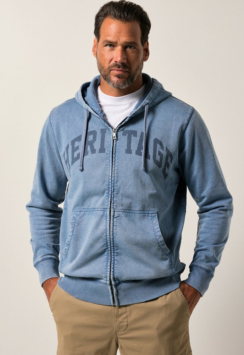 Light blue zip-up hoodie made of cotton blend, featuring a "HERITAGE" print, drawstring hood, and front pockets. Soft texture with ribbed cuffs.