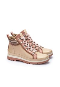 Botas de senderismo de caña alta con cuero beige y rosa dorado, cordones en contraste y una suela de goma gruesa. Presenta detalles metálicos y lengüetas de agarre.