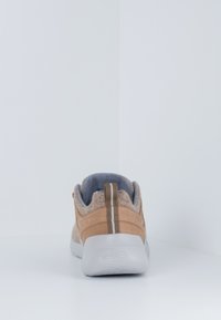 Beige Sneaker mit strukturierter Oberfläche, grauen Akzenten und Gummisohle. Besitzt einen braunen Streifen und ein Logo an der Ferse.