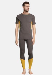 Mænds atletiske outfit inkluderer en grå t-shirt med korte ærmer og gule sidelogoer samt matchende grå leggings med gule farveblokke ved anklerne.