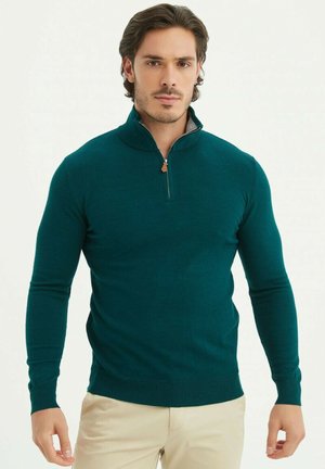 Pull en maille teal avec un col haut, une fermeture éclair sur le devant et des poignets côtelés. Fabriqué à partir d'un tissu doux, il présente une coupe ajustée et une texture lisse.