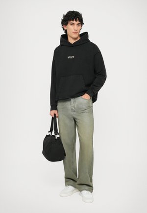 Felpa nera con cappuccio e tasca frontale, jeans verde chiaro, sneakers bianche e una borsa nera. Look casual con una texture morbida.