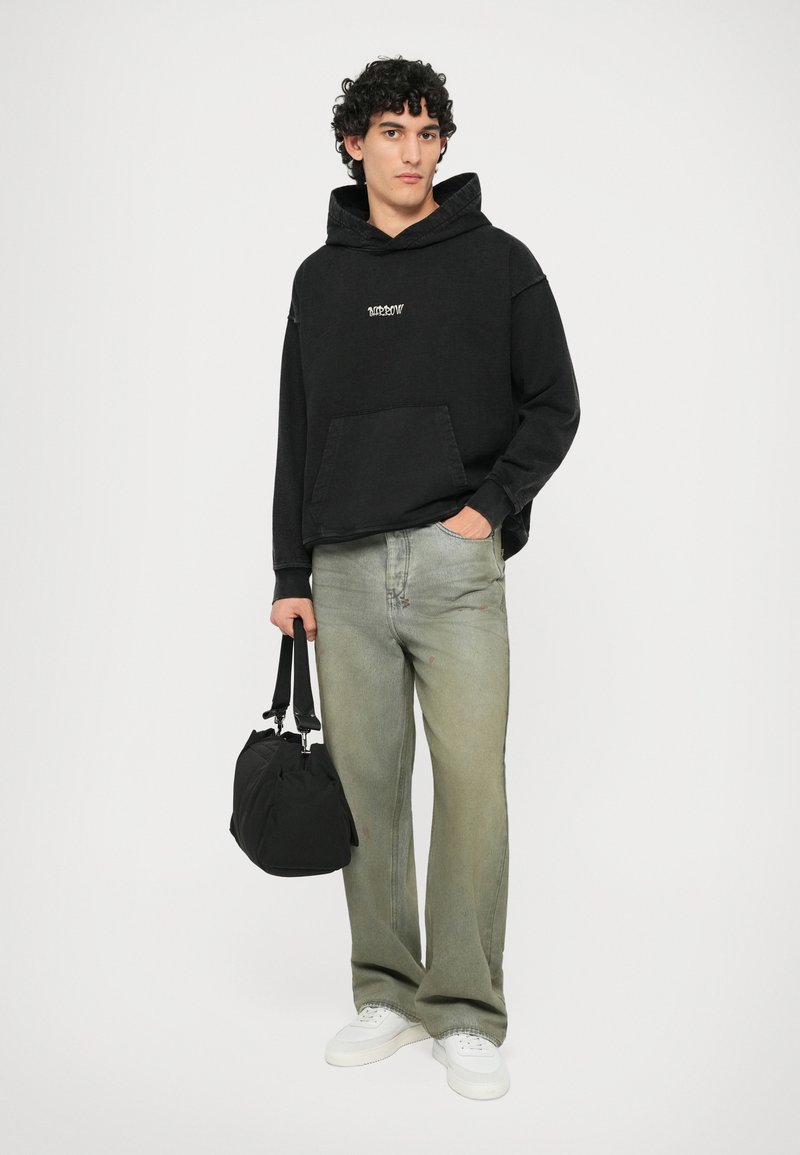 Felpa nera con cappuccio e tasca frontale, jeans verde chiaro, sneakers bianche e una borsa nera. Look casual con una texture morbida.