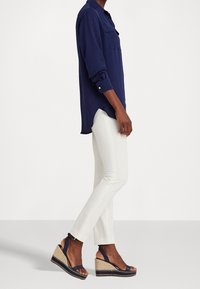 Marinblå skjorta med knappar, vita byxor och kilklackssandaler med marinblå remmar och en naturligt vävd bas. Skjortan har en ficka och uppvikta ärmar.