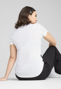 T-shirt bianco a maniche corte dal design aderente, texture liscia, con orlo rotondo, abbinato a pantaloni neri larghi e sneakers bianche.