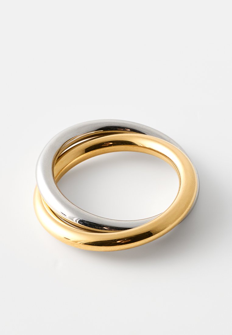 Deux anneaux entrelacés, l'un en argent et l'autre en or. Surface lisse et polie avec un extérieur arrondi et un intérieur creux. Aucune inscription visible.