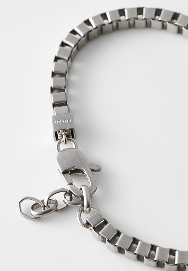 Silberne Metallkette mit rechteckigen Gliedern und einem Karabinerverschluss, teilweise rund auf weißem Hintergrund, Marke Fossil sichtbar am Verschluss.