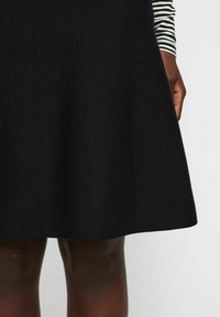 Schwarzer A-Linien-Rock aus strukturiertem Strickstoff, der nahtlos zu einem einfarbigen Saum übergeht. Kombiniert mit einem gestreiften Langarmshirt.