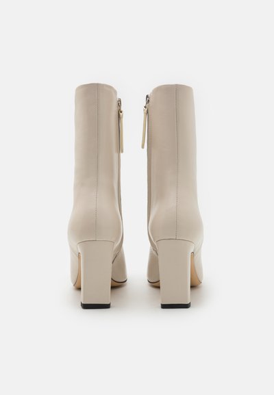 Beige enkellaarsjes met een gladde leren afwerking, vierkante hakken en zijritsen. Kenmerkt zich door een minimalistisch design met subtiele stikseldetails.